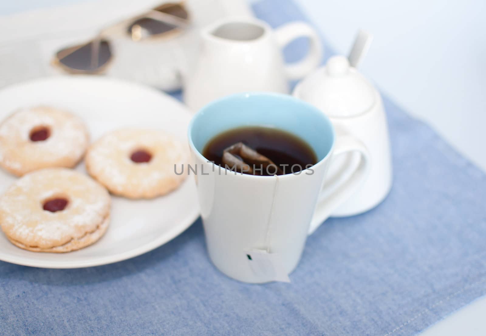 Mug of Tea, Cookies, Cream Pot, Sugar Basin and Newspapers with Glasses on Table