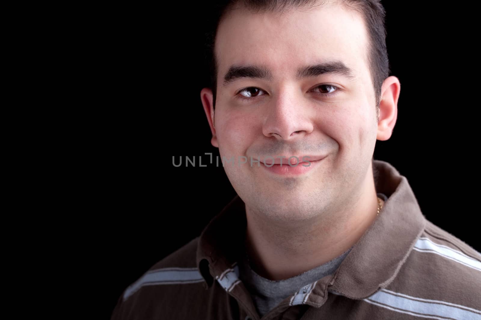 A happy smiling man in his late twenties isolated over a dark black background.  Low key lighting technique.