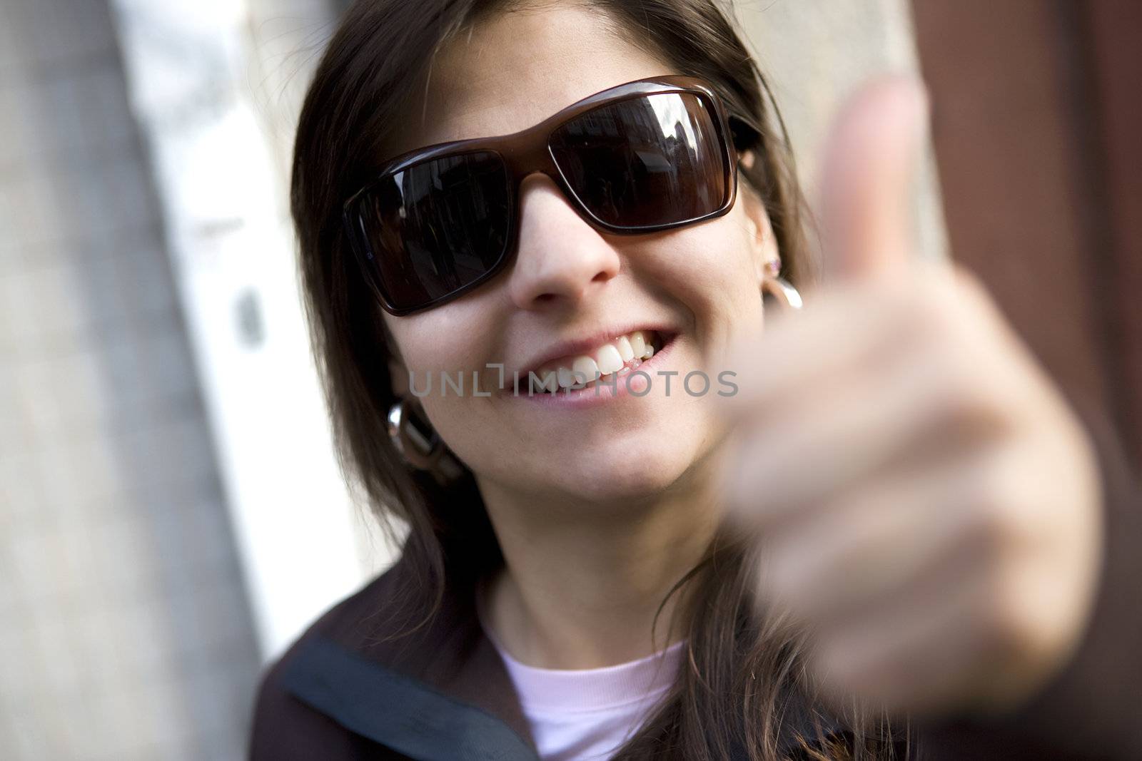 Portrait of beautiful casual woman with thumbs up - selective focus on the sunglasses