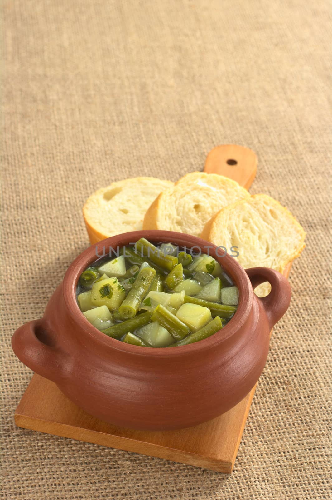 Green bean and potato hotpot in rustic bowl with baguette slices on wooden board (Selective Focus, Focus on the first half of the hotpot) 
