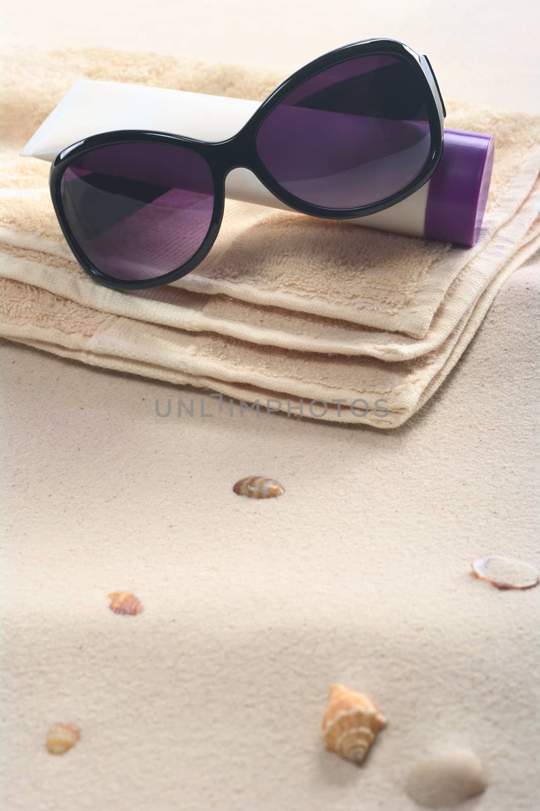 Beach setting with sunglasses, suncream and towels on sand with shells (Selective Focus, Focus on the sunglasses)