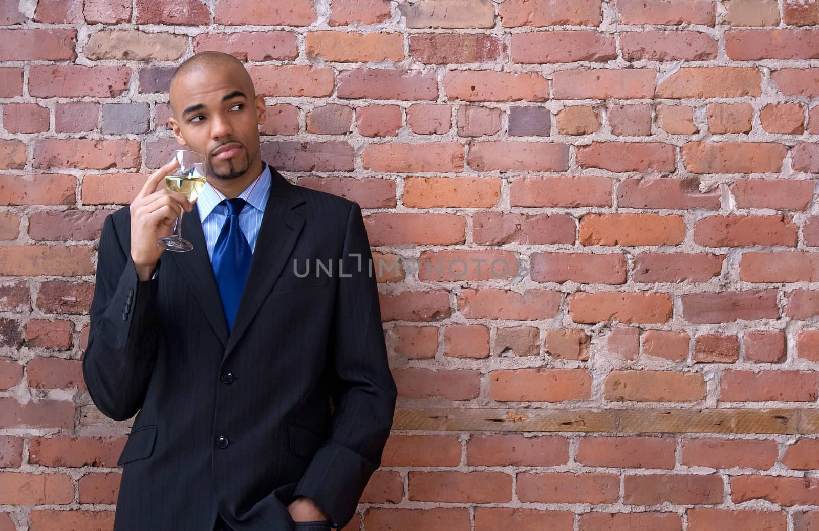 Young business man leaning against the brick wall, thinking and drinking wine.