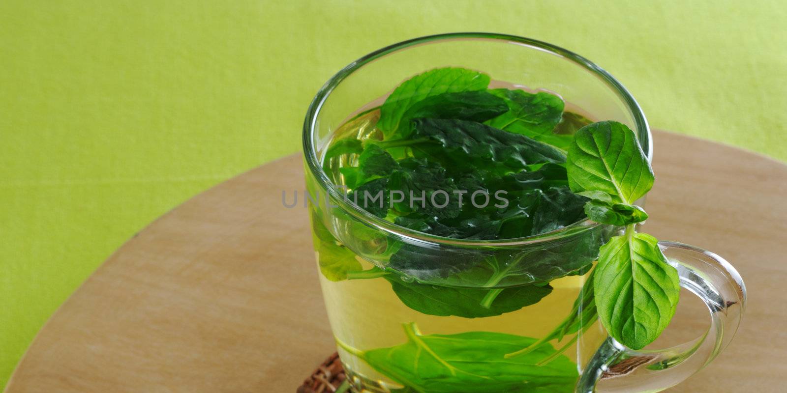 Fresh mint tea in glass cup with mint leaves on wooden board and green tablecloth (Selective Focus)