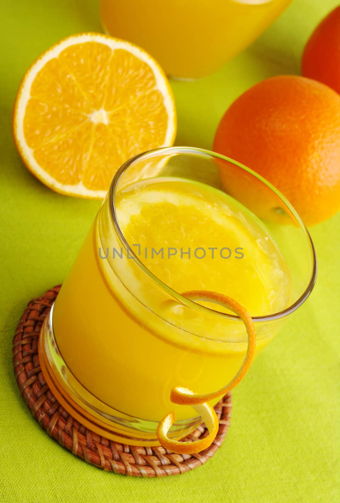 Fresh orange juice with orange slice in glass and oranges in background on green table mat (Selective Focus)