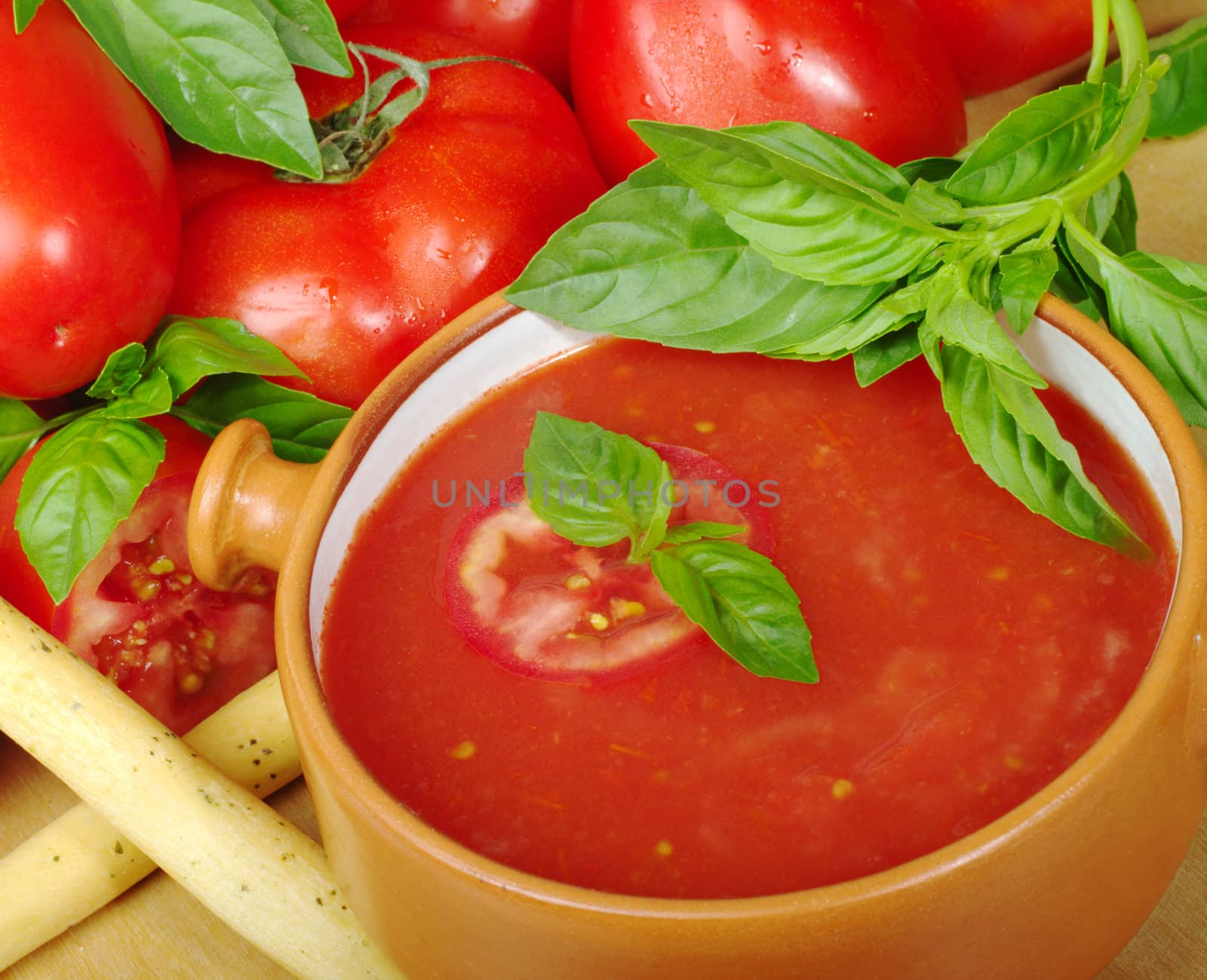 Tomato soup in bowl in between tomatoes and basil (Selective Focus)