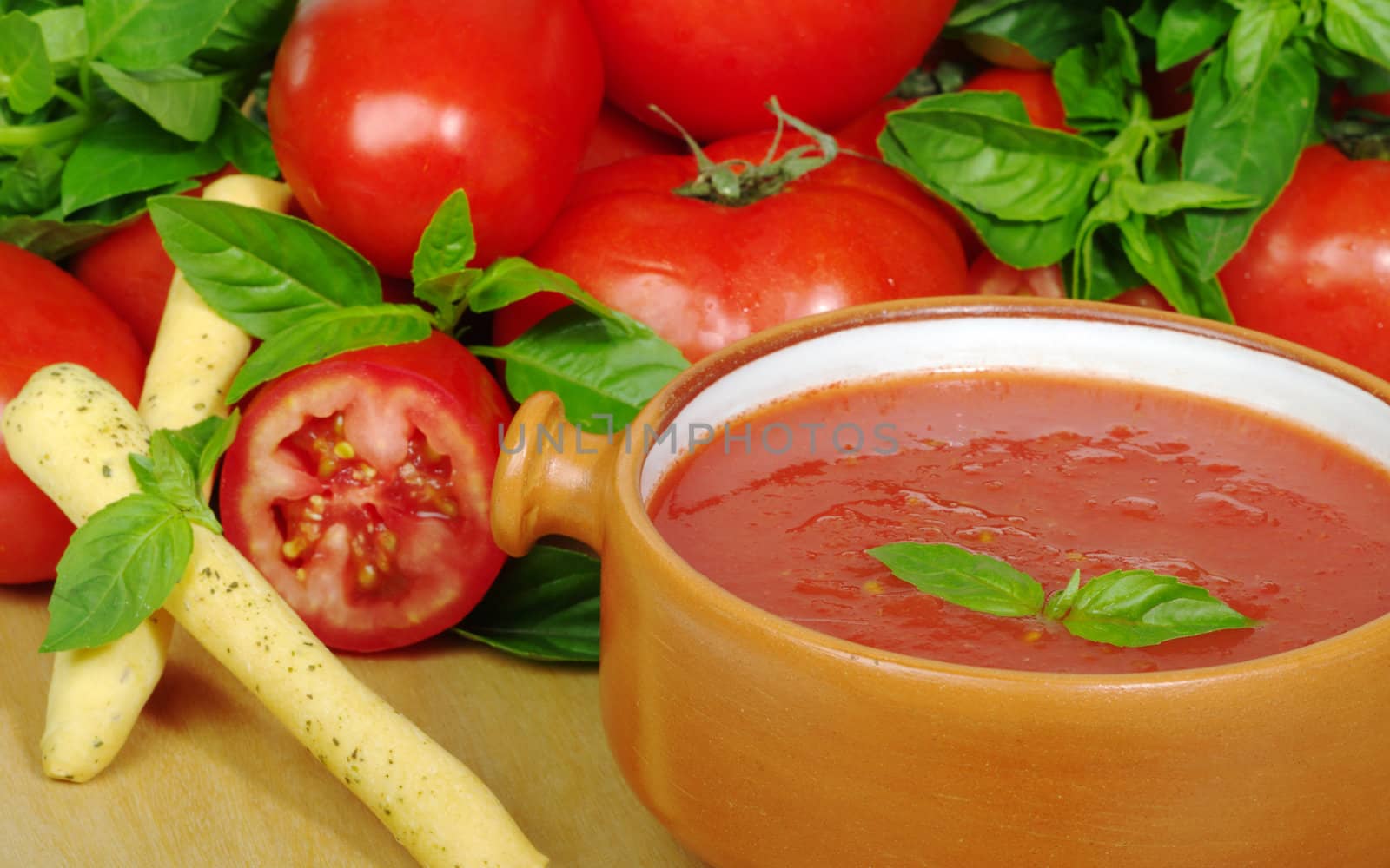 Tomato soup in bowl in between tomatoes and basil (Selective Focus)