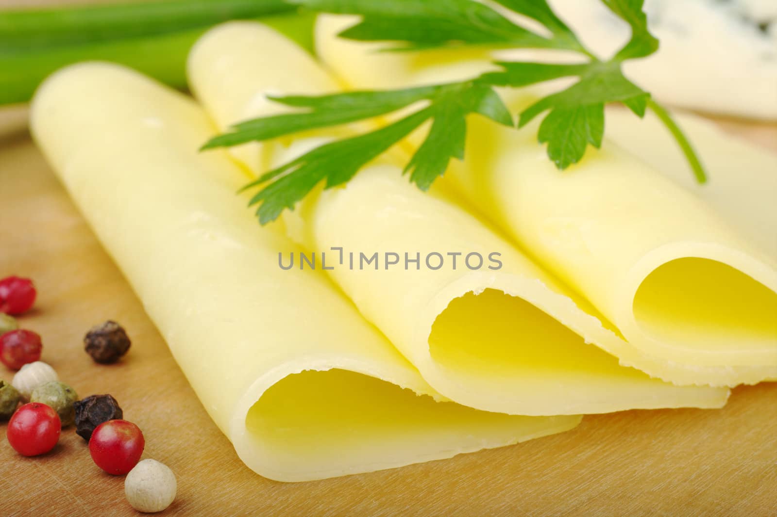 Slices of cheese on wooden plate with parsley and peppercorns