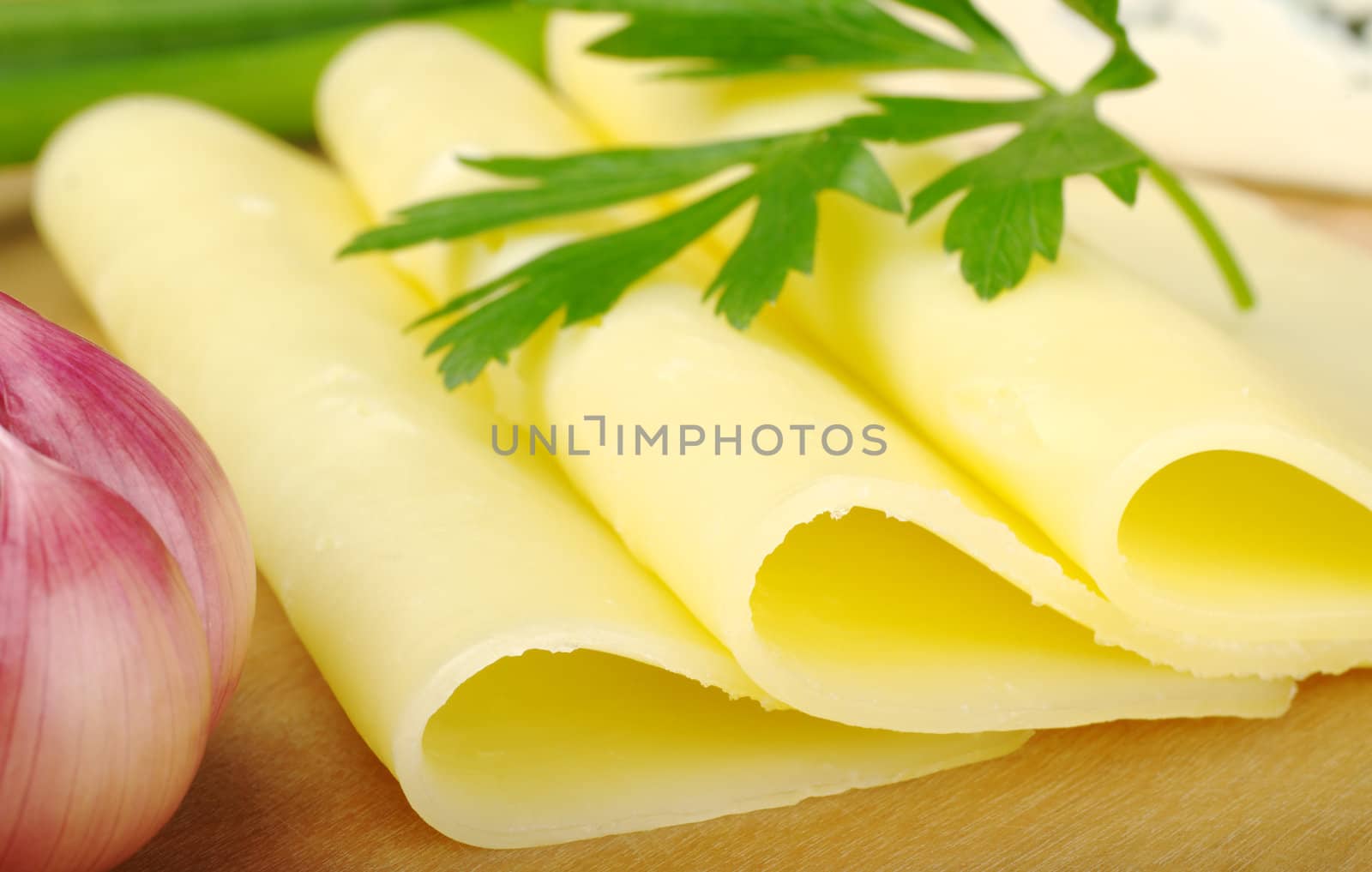 Slices of cheese on wooden plate with parsley and garlic