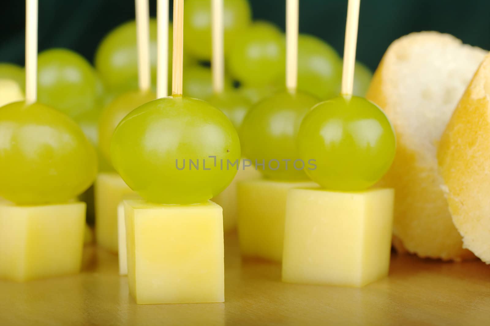 Cheese, grapes and baguette on a wooden board with green background (selective focus)