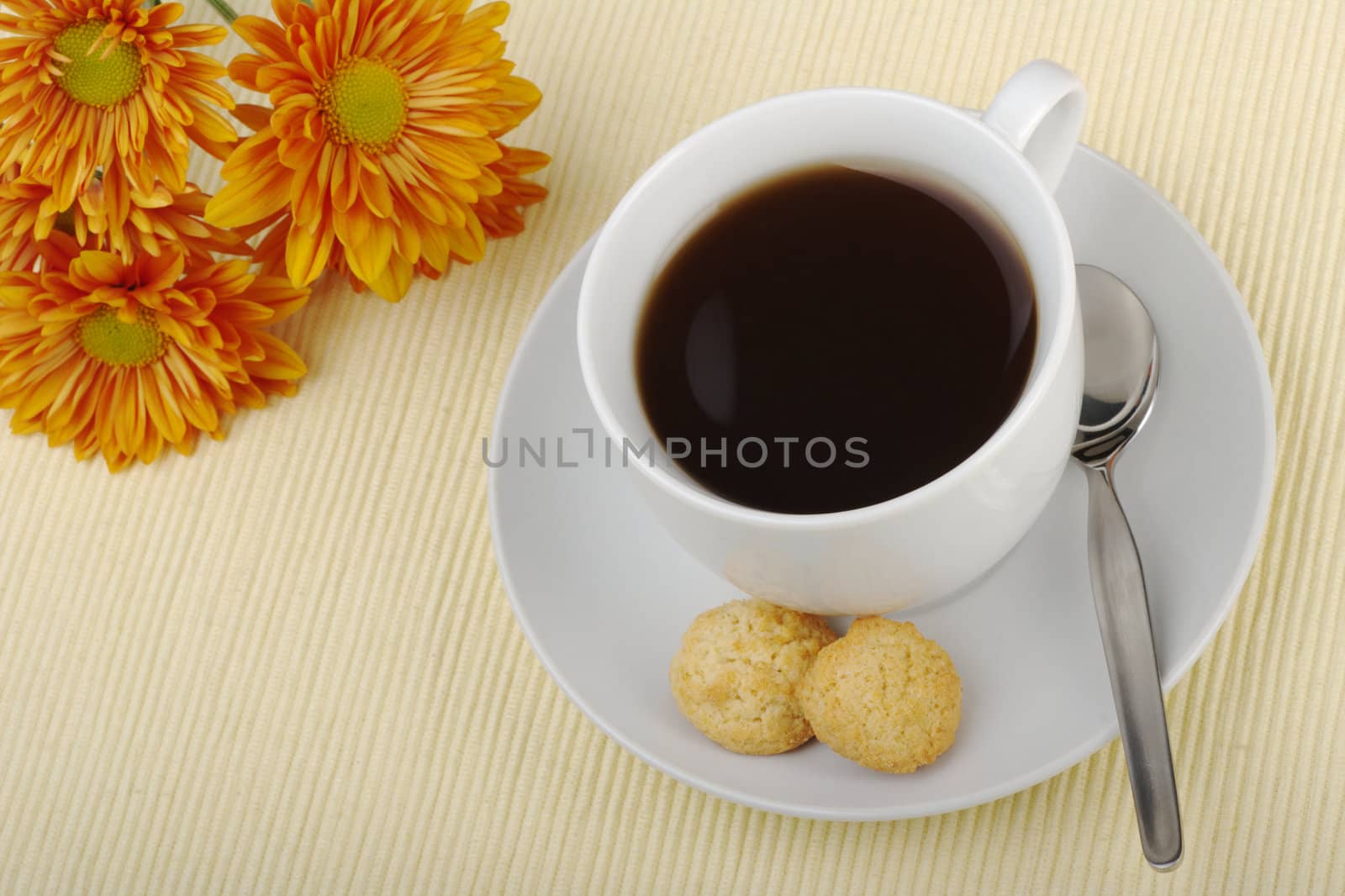 Blacktea in cup with saucer, teaspoon, biscuits and orange flower in the background on tablemat (Selective focus)