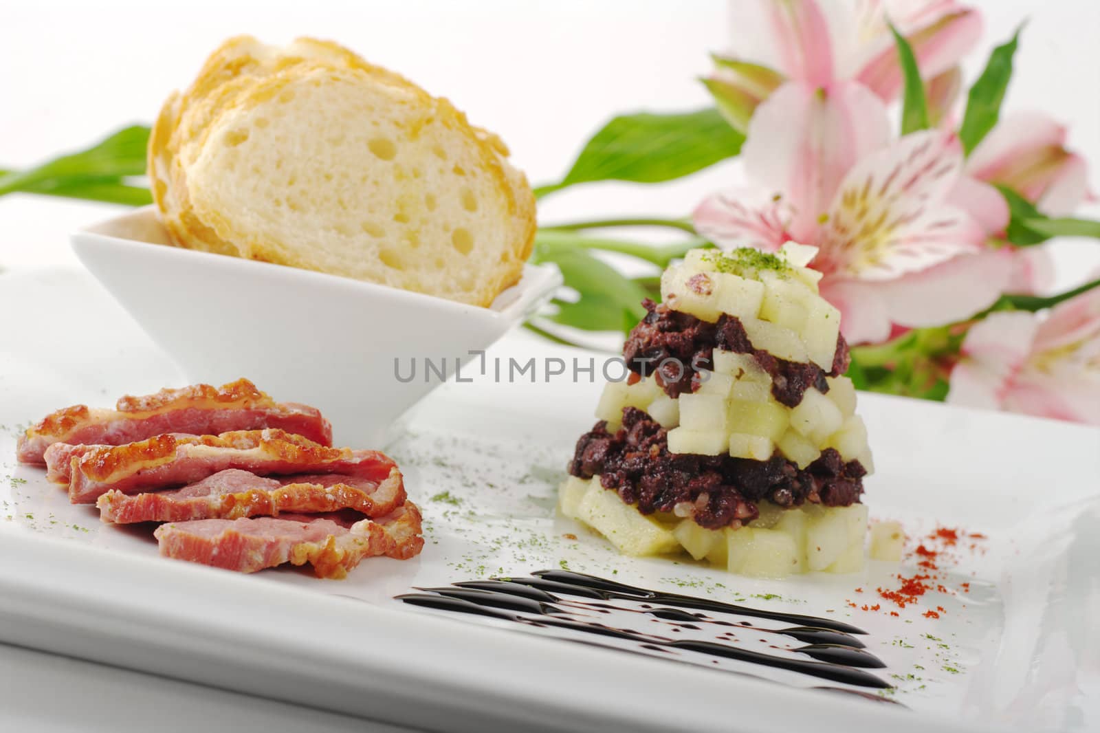 Starter with Duck Meat, Apples, Blood Sausage and Baguette, on white plate with Flower in Background (Selective Focus,Tilted)