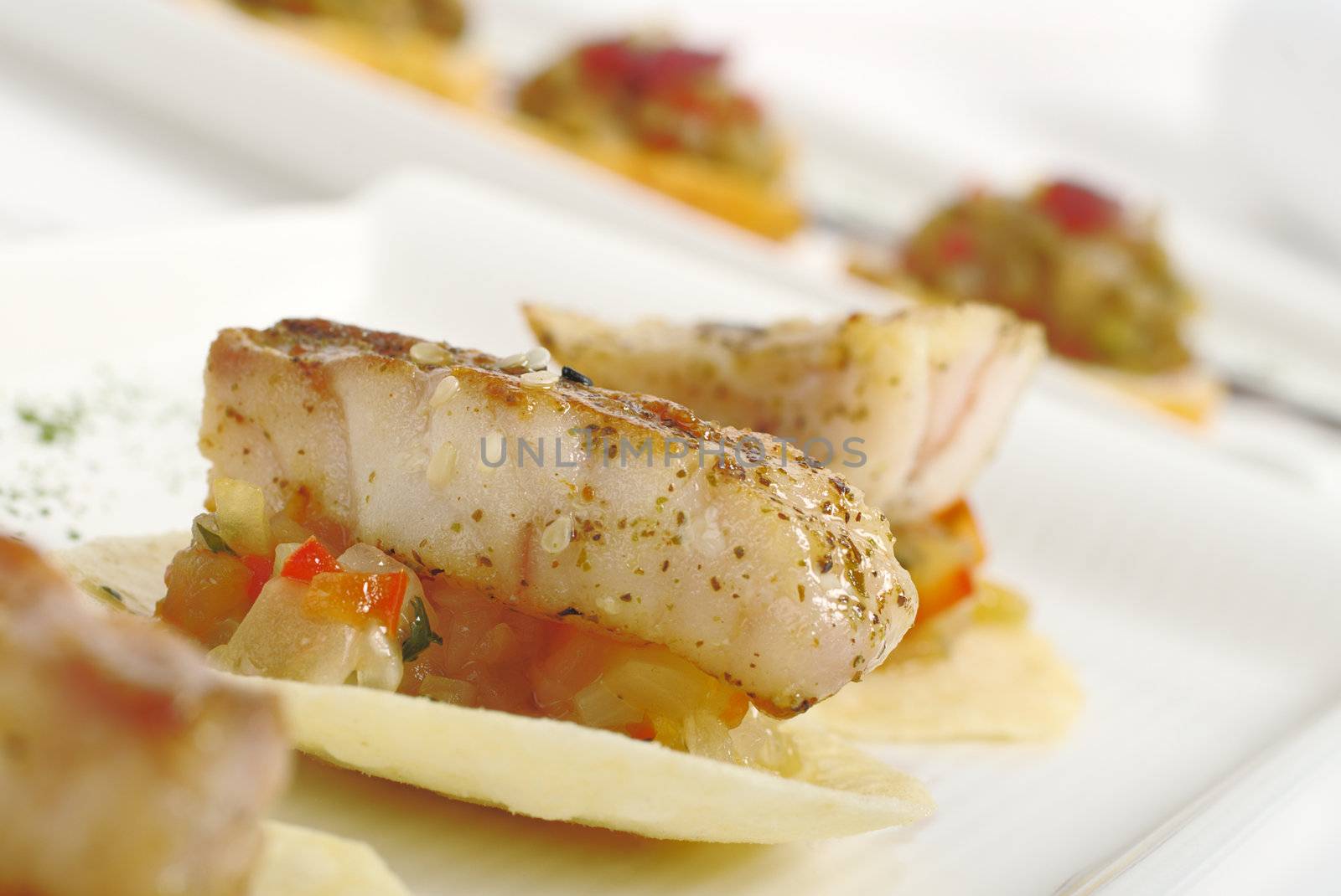 Appetizer: Piece of Fish on Vegetables and Chip with other appetizers in the background (Selective Focus)