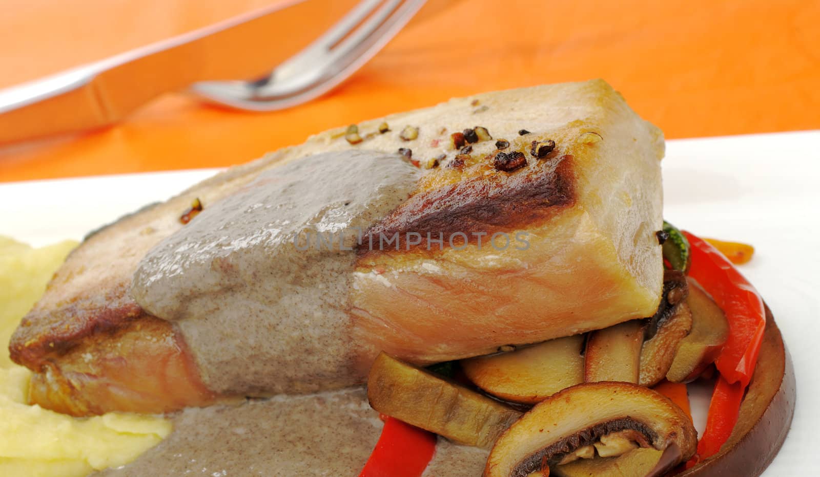 Main Dish: Mediterranean Tuna with mashed potato, gravy and vegetables with orange background and cutlery (Selective Focus)