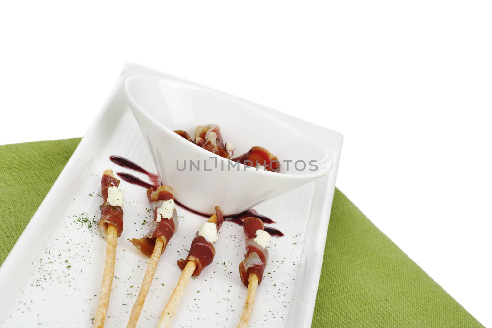 Thin ham slices wrapped around thin bread sticks and served on a long plate on a green place mat (Selective Focus, Isolated) 