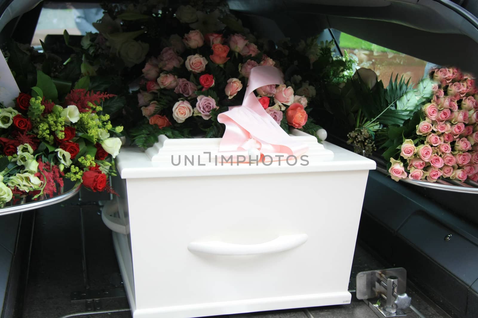 A white coffin, covered with flowers in a grey hearse