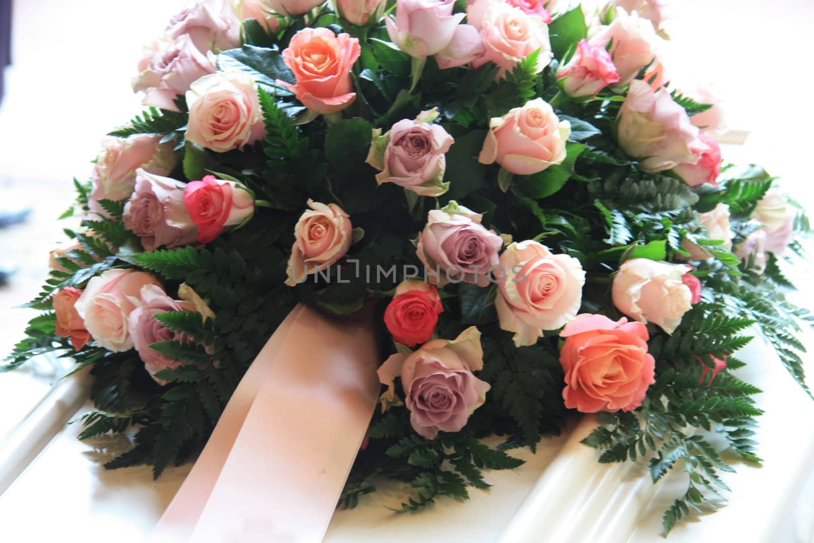 pink sympathy flowers with a pink ribbon on a white coffin