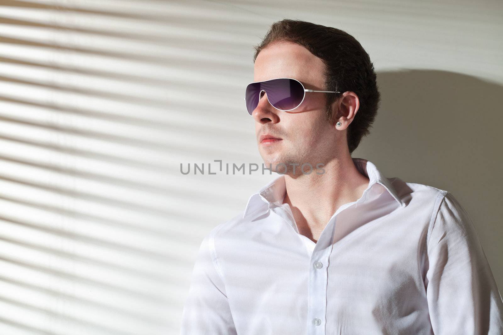 Man in sunglasses looks in the window; stripe shadows from the blinds