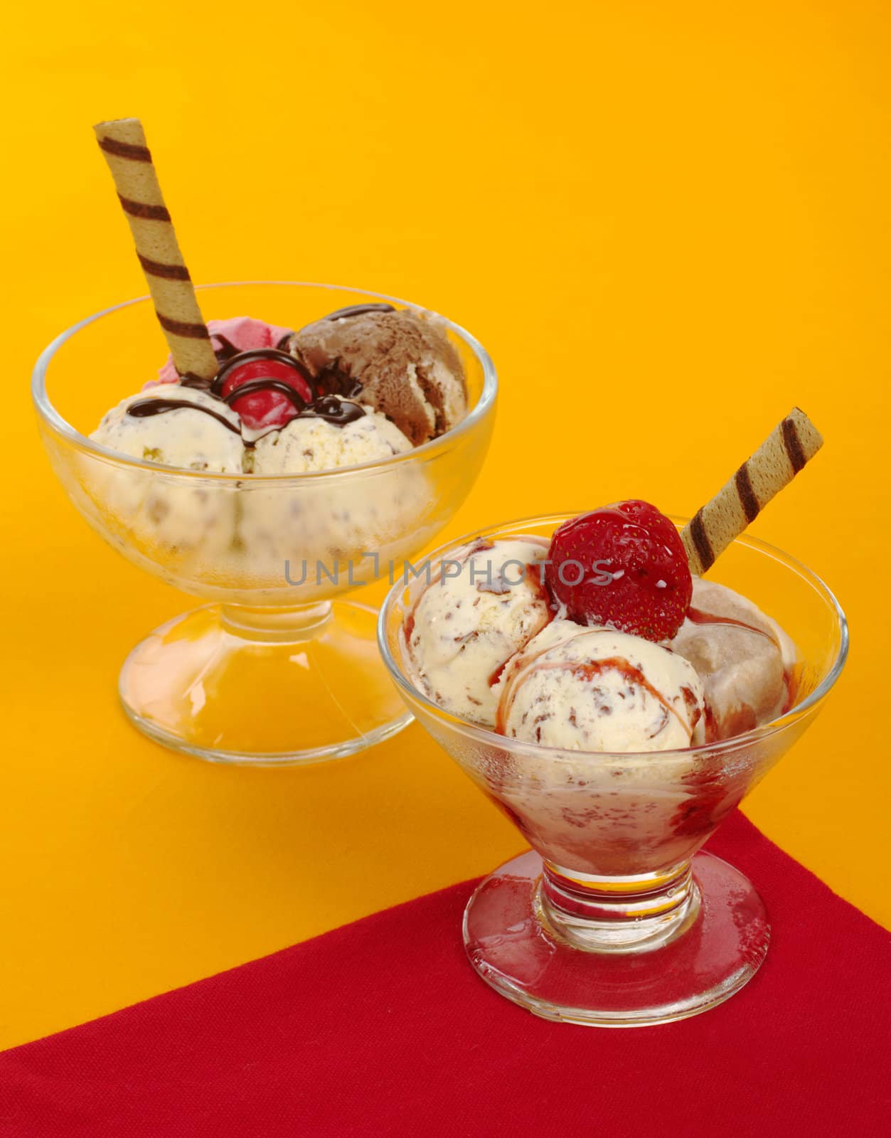 Ice-cream scoops in glass with syrup and wafer-rolls on red and orange (Selective Focus) 