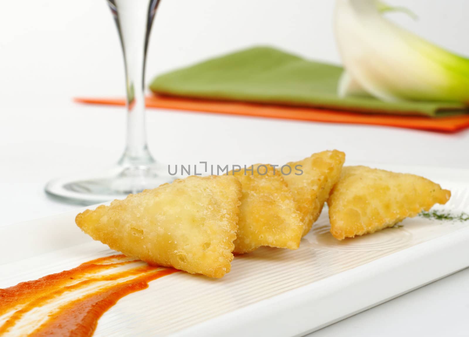 Appetizer: Empanada de Queso de Cabra (Pasty filled with goat cheese) with sauce, wine glass, napkins and arum lily (Selective Focus)