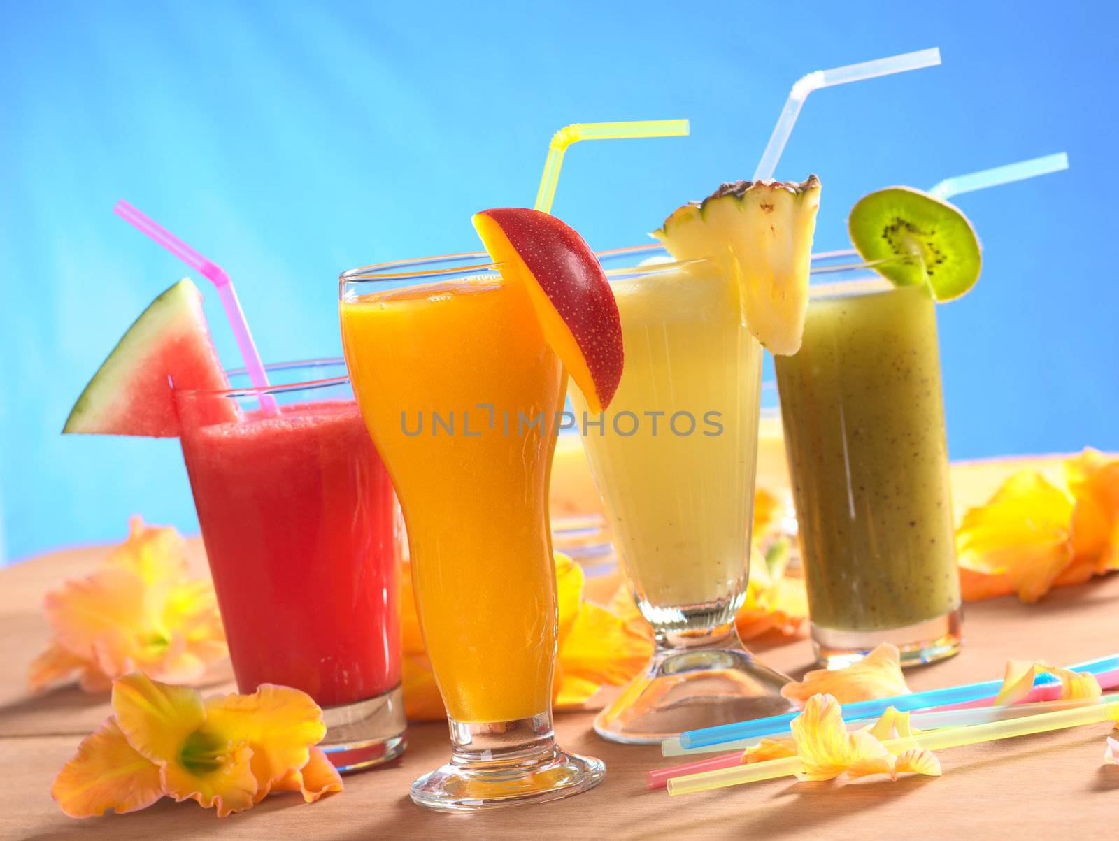 Mango, pineapple, watermelon and kiwi smoothie with drinking straws surrounded by gladiolus flower on wood (Selective Focus, Focus on the mango smoothie in the front)