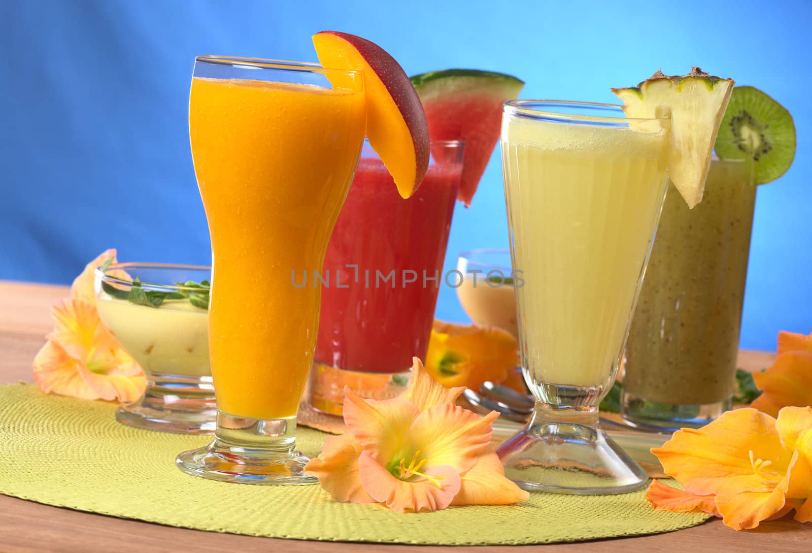 Mango, pineapple, watermelon and kiwi smoothies surrounded by gladiolus flower (Selective Focus, Focus on the mango and pineapple smoothies in the front)