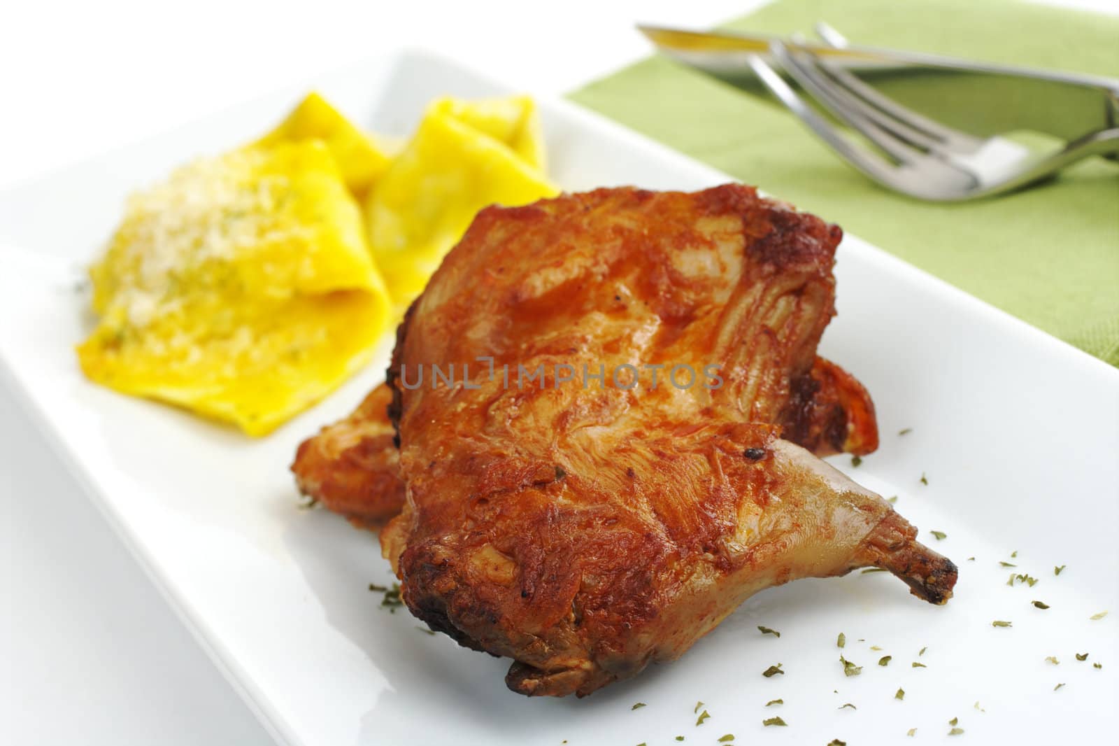 Main Dish: Guinea pig meat with ravioli on white rectangular plate with green table mat and cutlery in the background (Selective Focus)