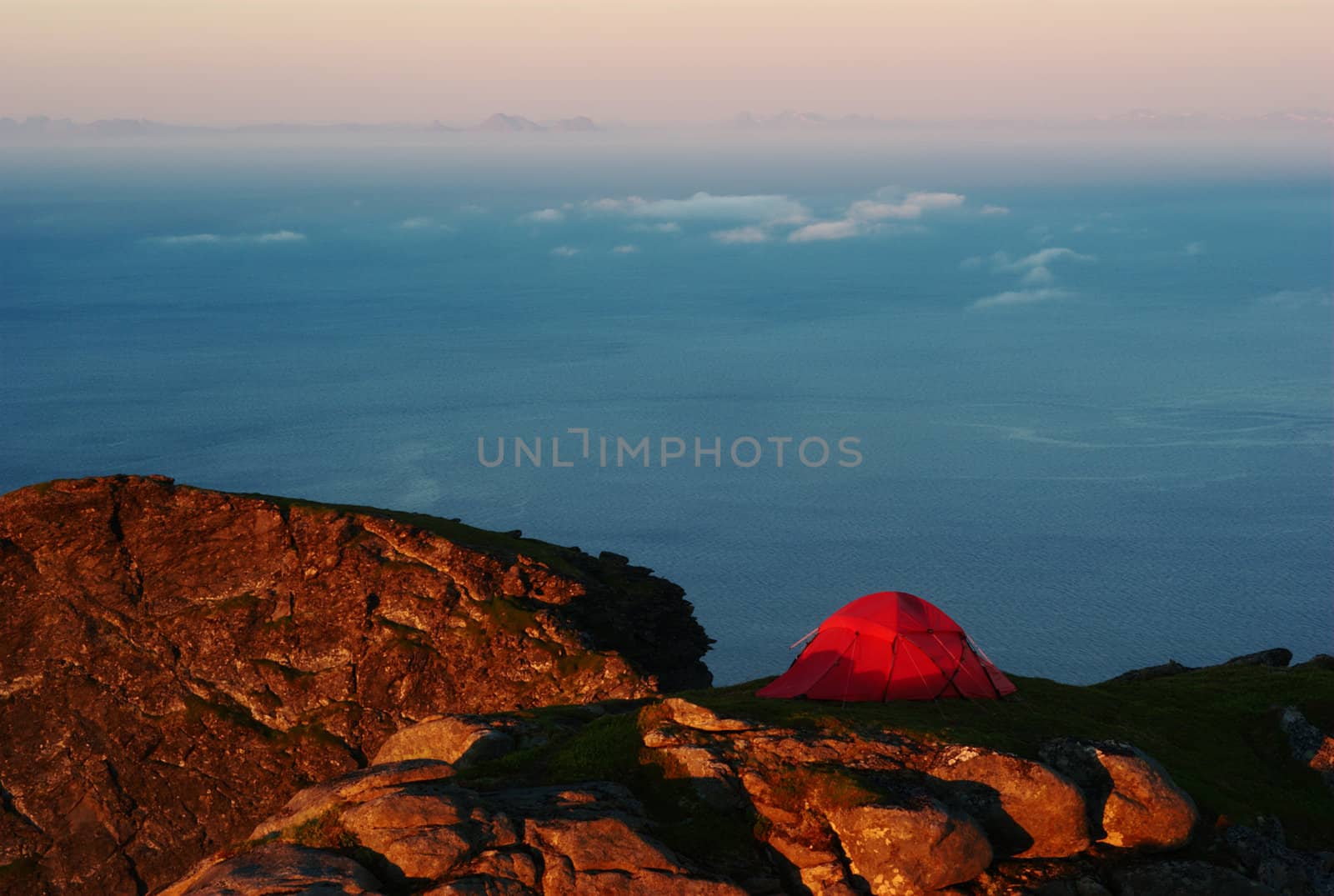 Red tent on mountain top at sunset overlooking the sea on the Lofoten in Norway