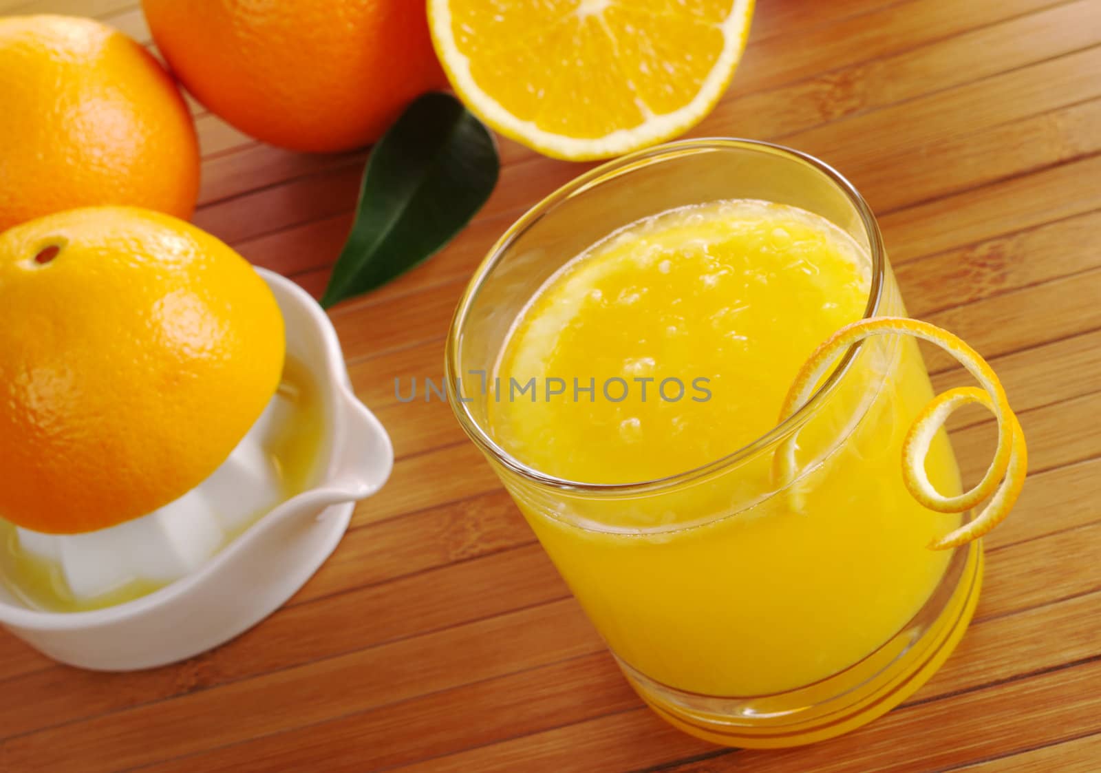 Fresh orange juice with orange slice in glass with squeezer and oranges in background on table mat (Selective Focus)