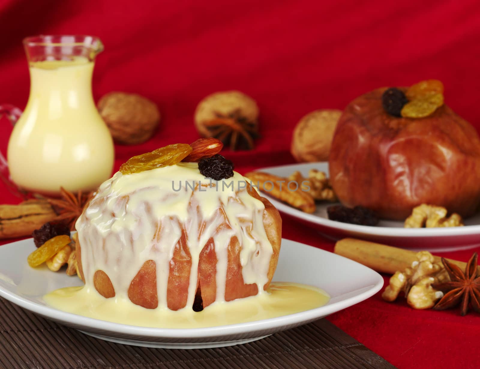 Baked apple with walnuts, raisins, almonds and vanilla custard on top on brown table mat and red fabric as background (Selective Focus) 