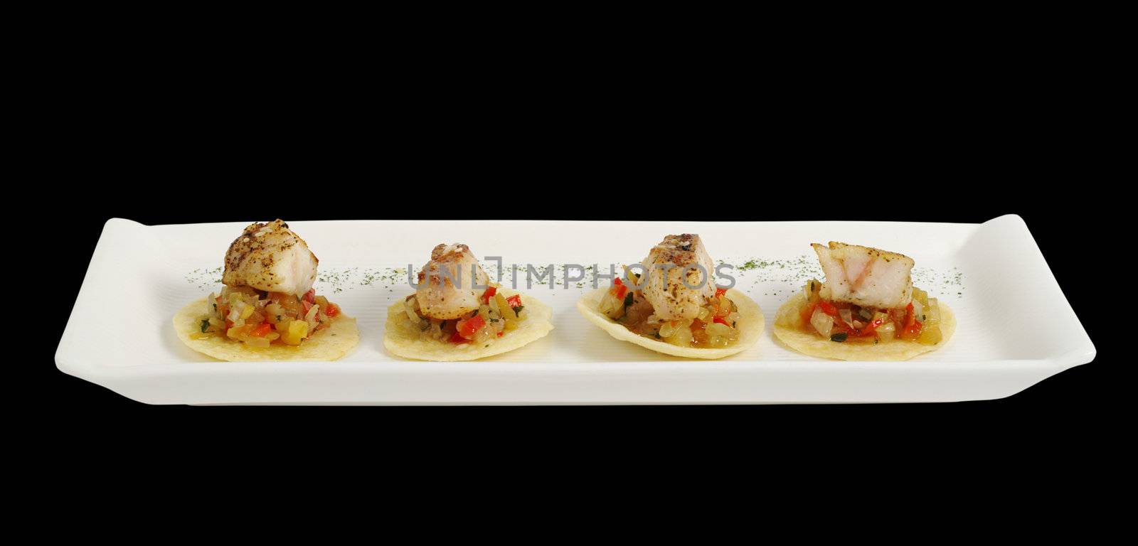 Appetizer: Pieces of tuna fish on vegetables and chips on rectangular white plate on black background (Isolated)