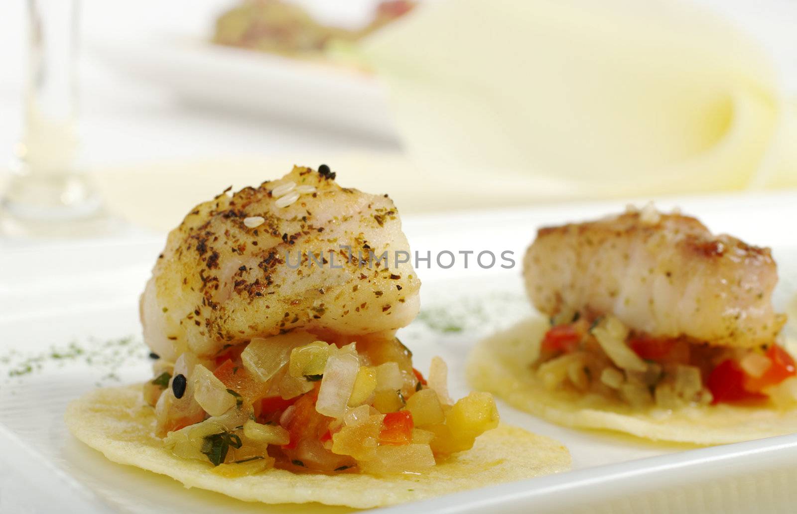 Appetizer: Piece of fish on vegetables and chip with glass and flower in the background (Selective Focus)