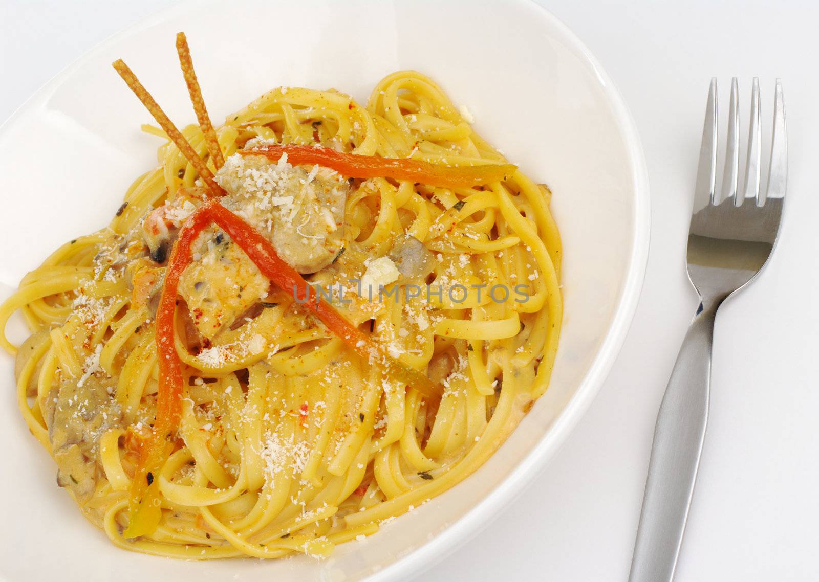 Fettuccine with chicken, mushrooms and red pepper garnished with salt sticks with a fork on white (Selective Focus) 