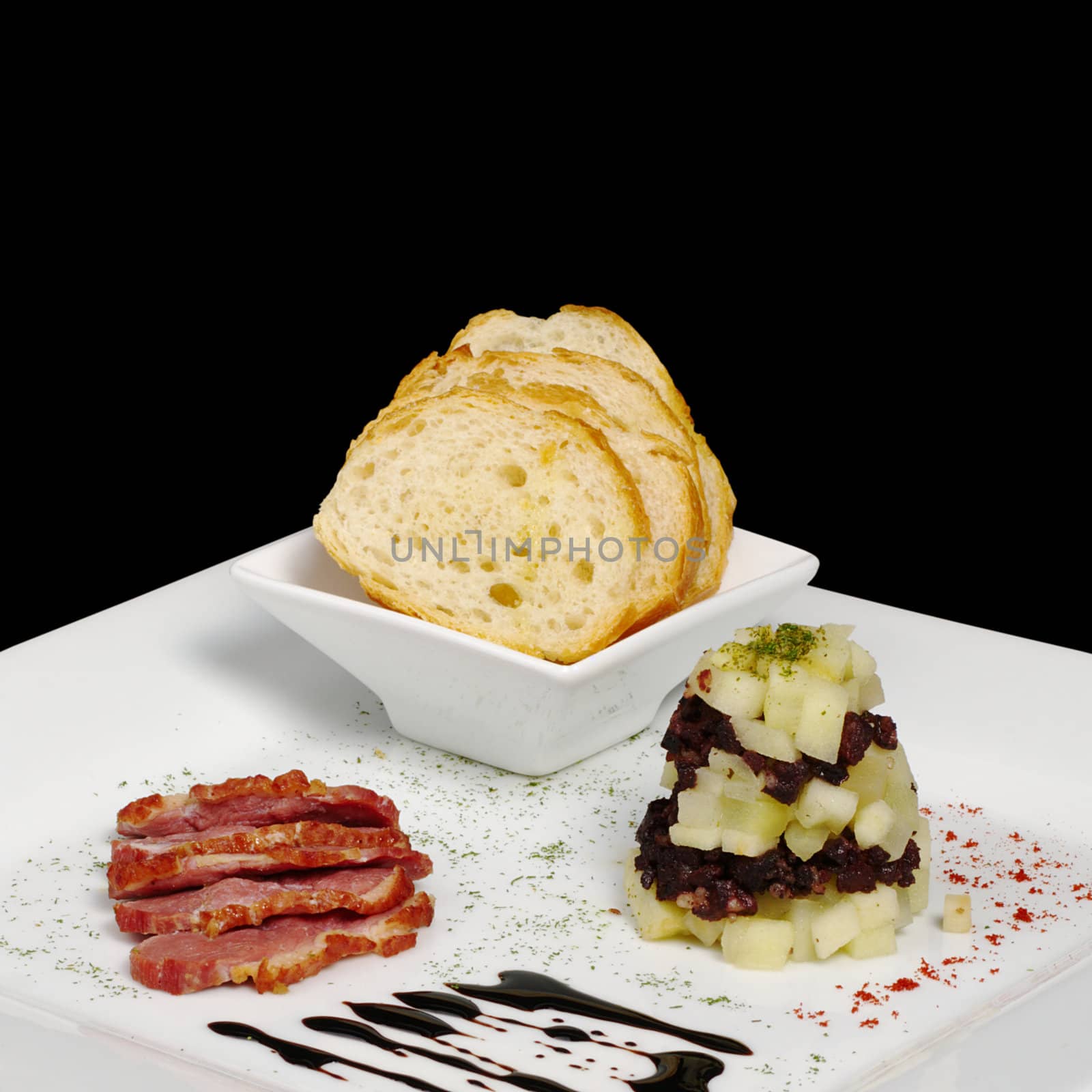 Appetizer: Duck meat, blood sausage, apples and baguette on white plate isolated on black