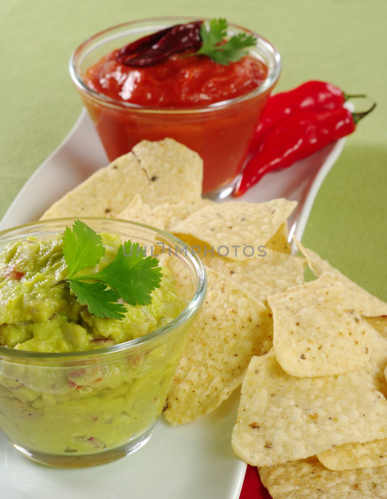 Guacamole with tacos and tomato-chili dip and chilis in the background on green (Selective Focus, Focus on the Guacamole)