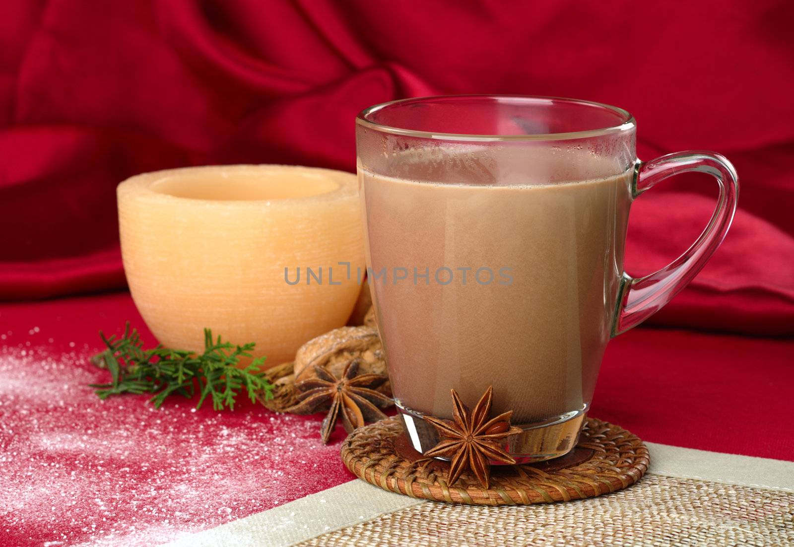 Hot chocolate in glass cup with anise, powder sugar, evergreen branch and candle in the background (Selective Focus, Focus on the glass cup)