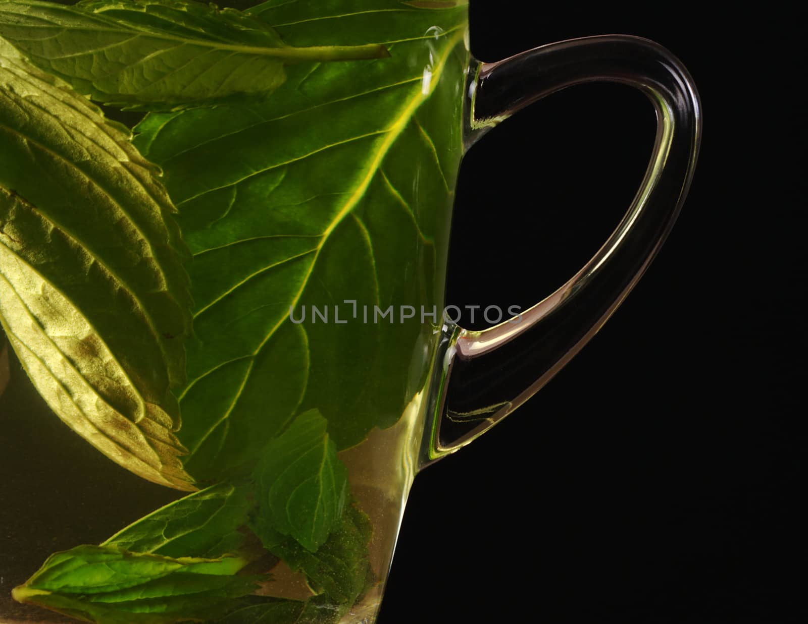 Fresh mint tea out of mint leaves in a glass cup photographed on black (Selective Focus, Focus on the handle of the glass) 