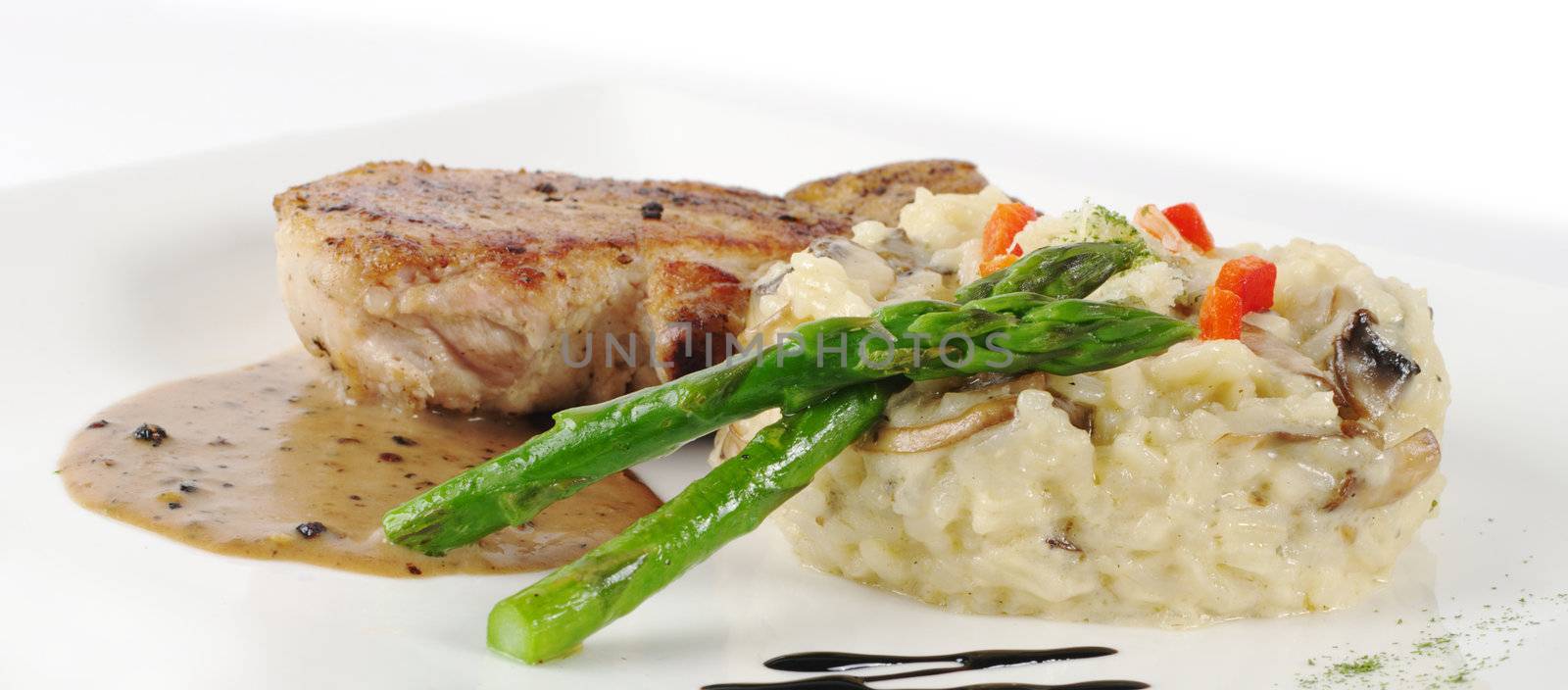 Risotto, green asparagus and meat with gravy on a garnished white plate (Selective Focus, Focus on the plane of the head of the asparagus)