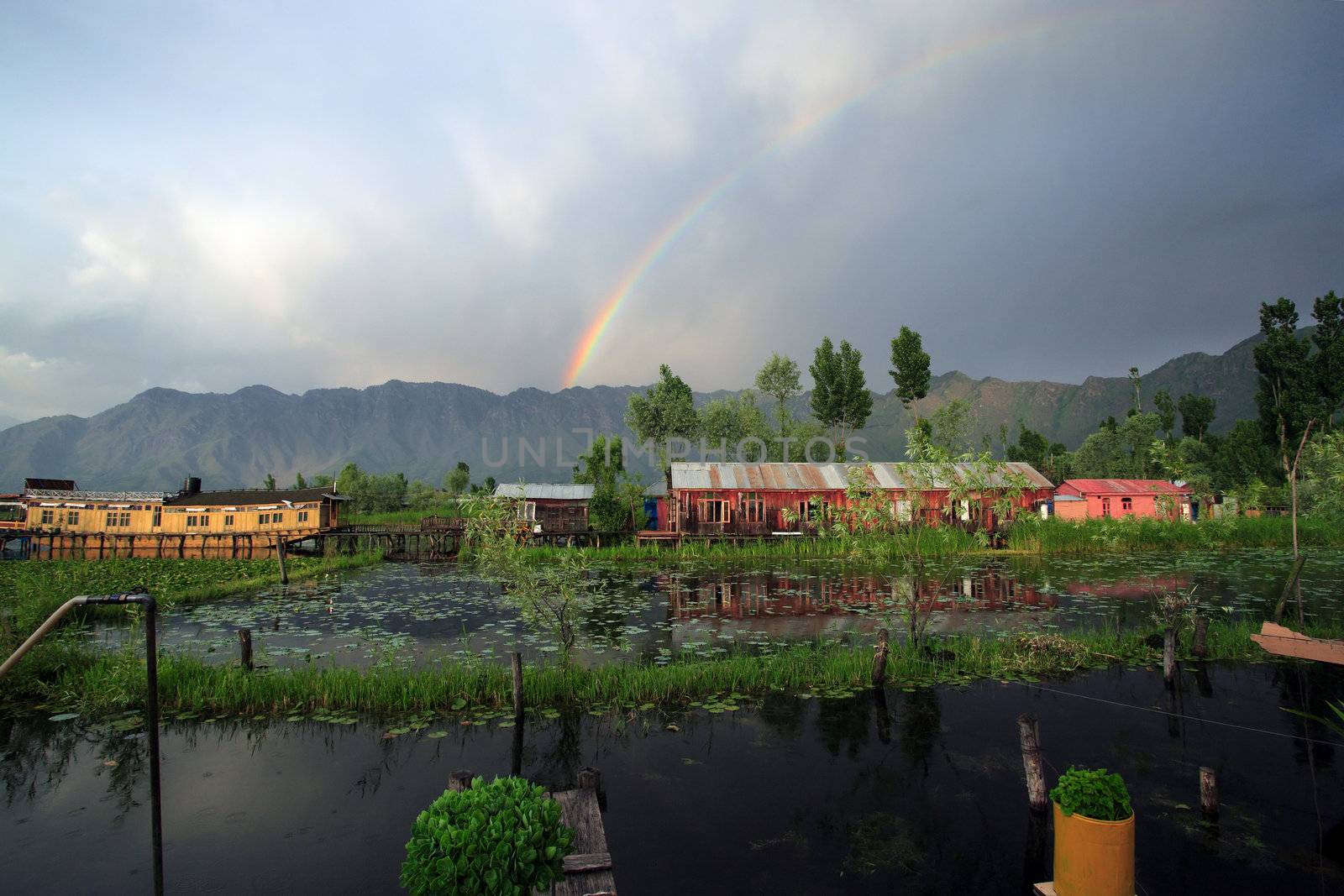 Houseboats in Srinigar, Kashmir (India) - after a light rain a rainbow appears in the distance with mountains as the backdrop.
