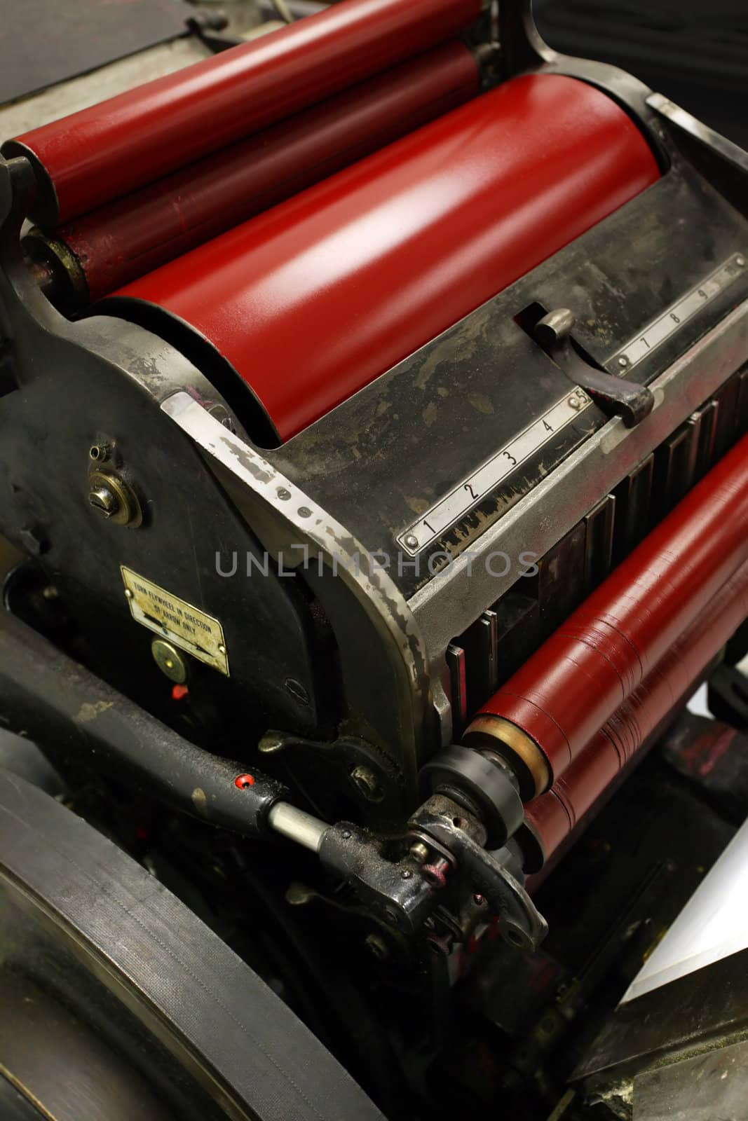 Image of an old windmill printing press / die cutter / numbering machine, with bright red ink on it's rollers.
