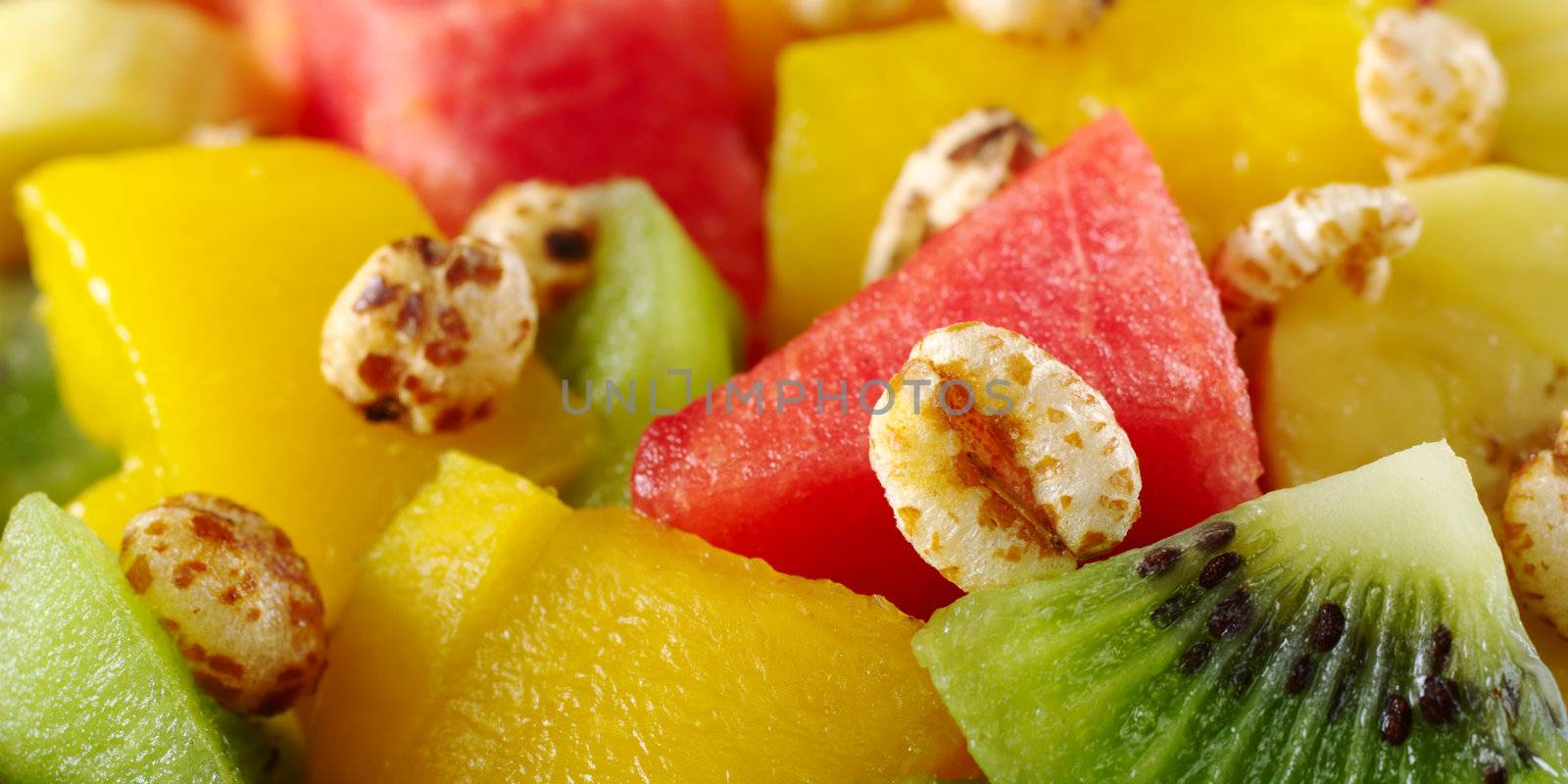Sweetened puffed wheat cereal on fresh and healthy fruit salad containing kiwi, watermelon, mango and banana (Selective Focus, Focus on the puffed cereal on the top of the kiwi)