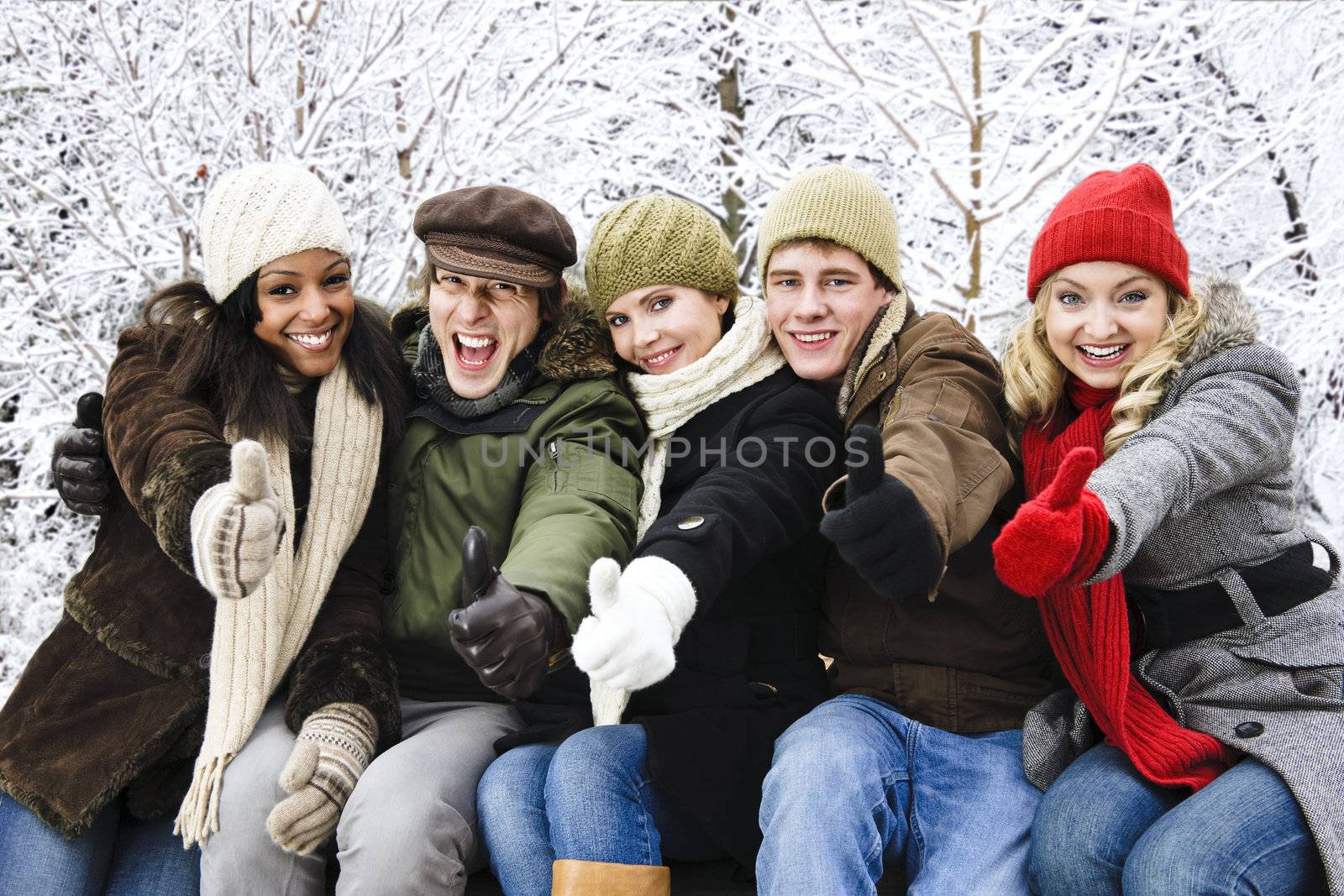 Group of diverse young friends showing thumbs up outdoors in winter