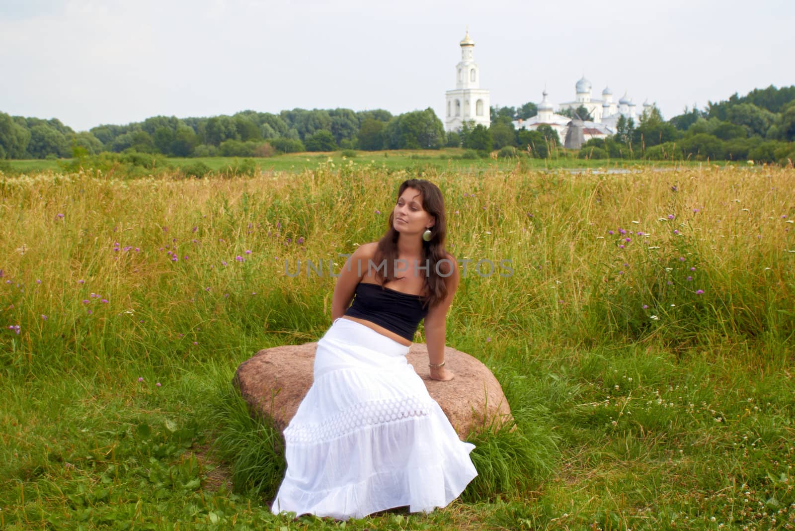 Pretty woman sits on field stone with monastery on background