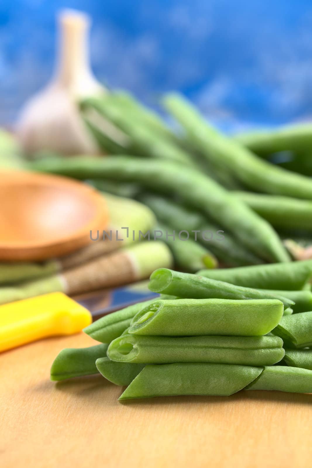 Raw cut green bush beans on wooden board with a kitchen knife, bean pods and garlic in the back (Selective Focus, Focus on the three beans lying on each other) 