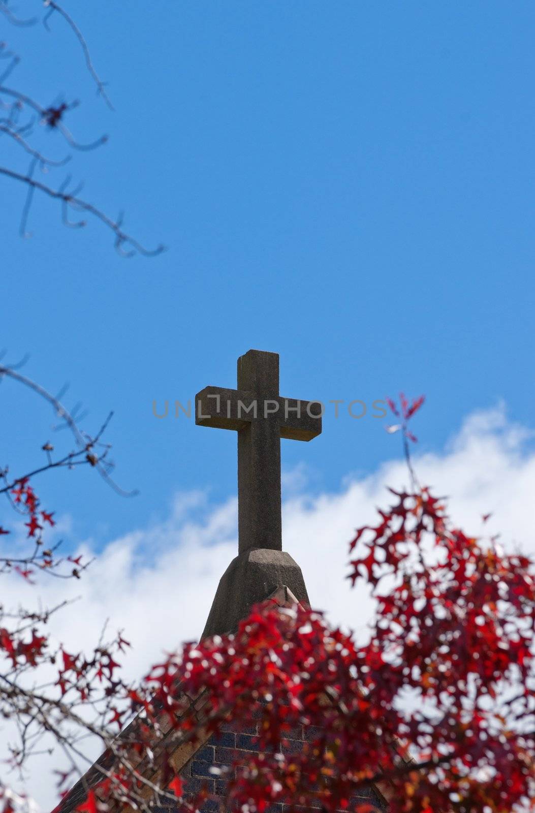 cross on church or chapel through red autumn fall leaves