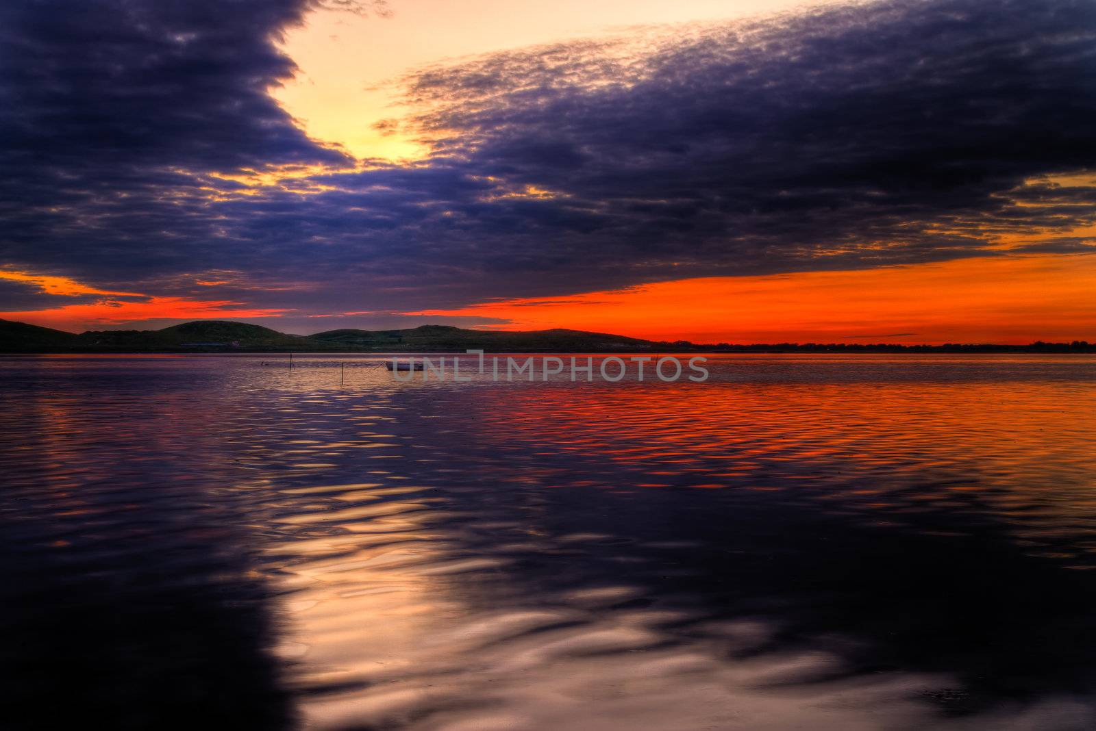 Scenic view of small fishing boat at sunset with cloudscape background.