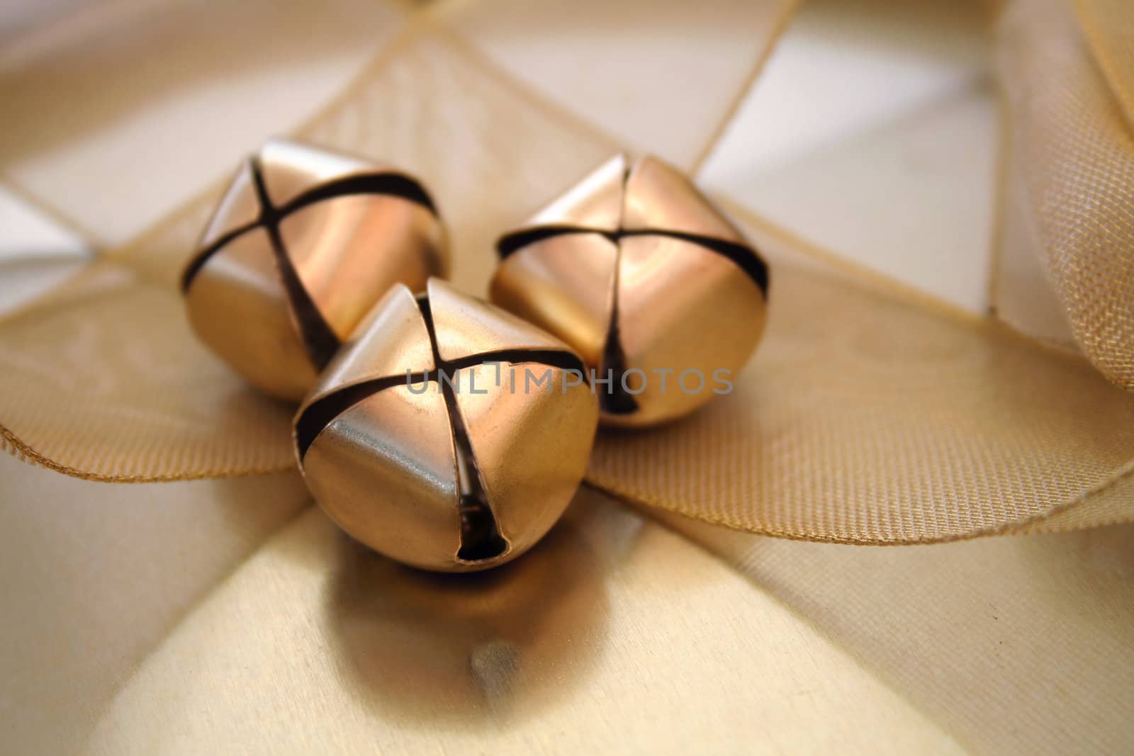 Three gold christmas bells sitting on a gold mesh ribbon.