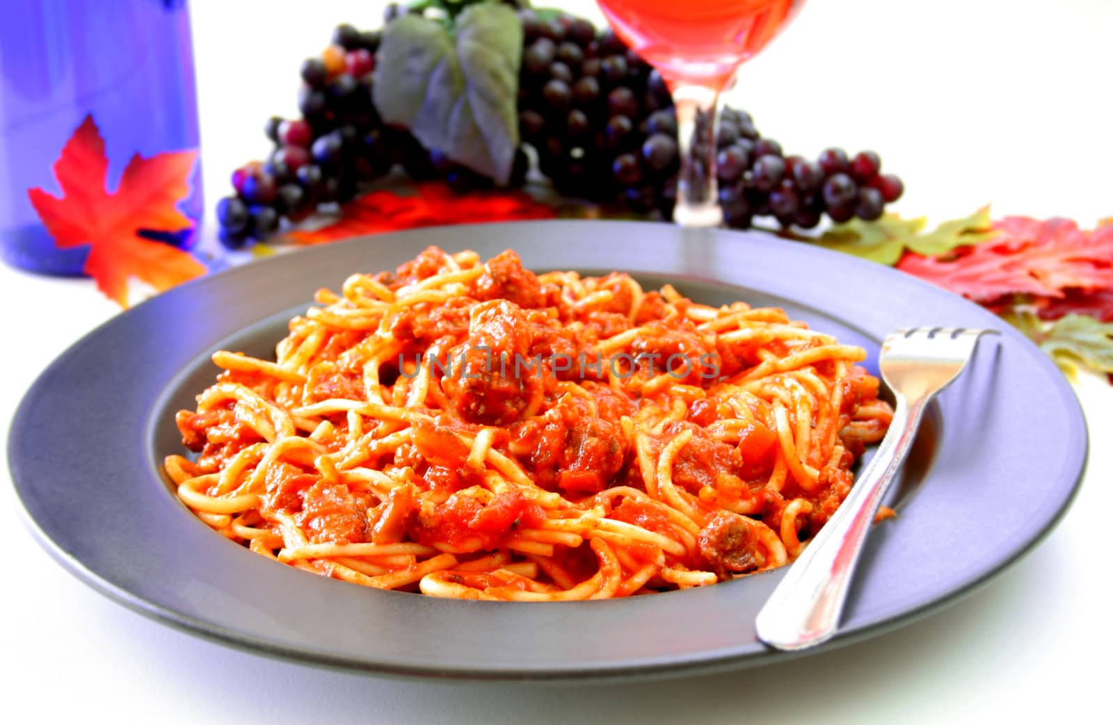 A plate of spaghetti with a glass of wine and wine bottle in the background.