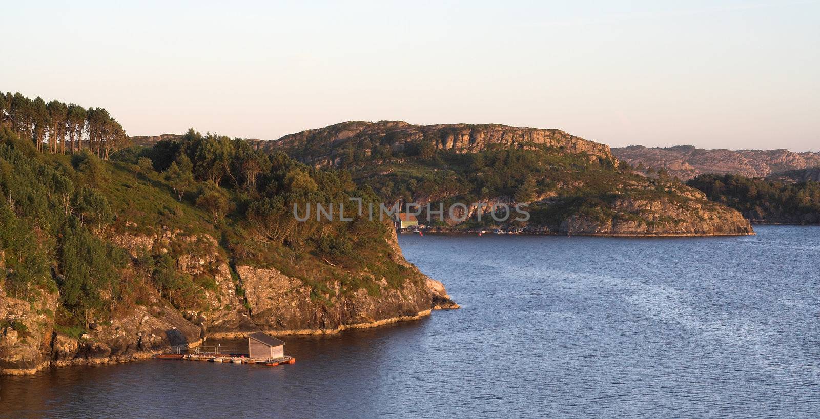 Rocky sea coast in sunset - Norwegian fjords; clear sky, still water with ripples