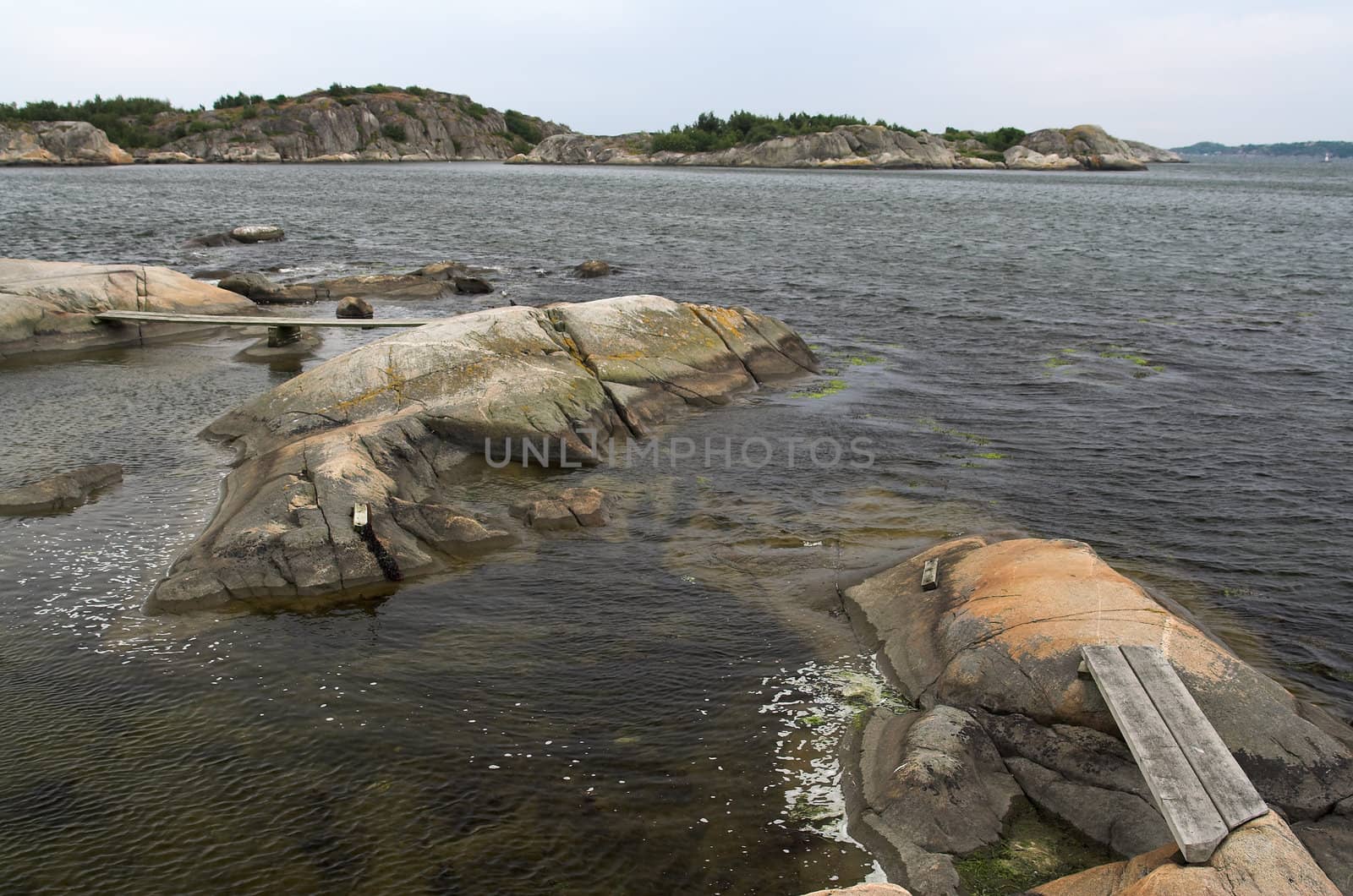 Rocks in the sea, connected by a wooden foot path; a rocky island in the background. Western Swedish coast.