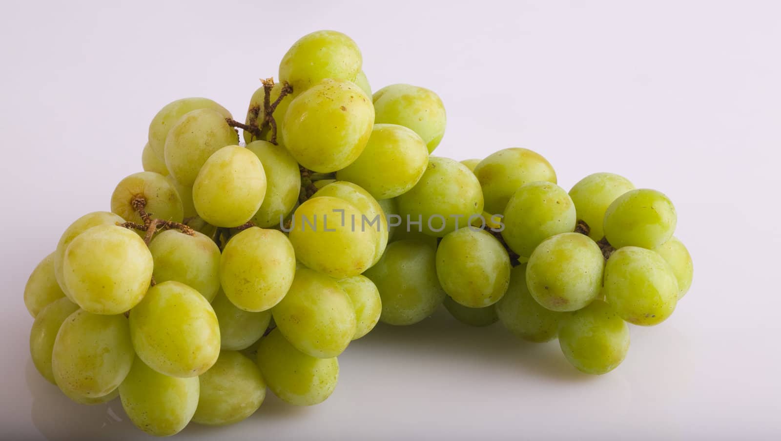 A green grape bunch on a white reflective background